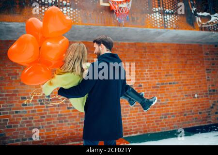 kaukasischen Mann Spinnen mit schönen Freundin in den Händen. Schönes Paar genießen zusammen, schöne Dame mit roten Luftballons in den Händen. Liebe Co Stockfoto