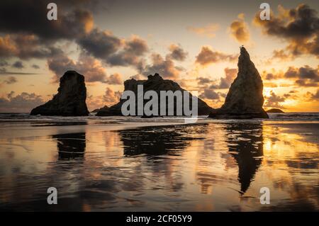 Dramatische Wolken über den Meeresstapeln in Oregon bei Sonnenuntergang mit Spiegelung im Sand. Stockfoto