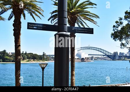 Ein Wegweiser in den Royal Botanical Gardens. Im Hintergrund über die Farm Cove ist das Sydney Opera House und die Harbour Bridge zu sehen. Stockfoto