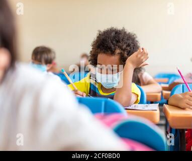 Schuljunge trägt Maske und Studie im Klassenzimmer Stockfoto