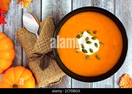 Kürbissuppe mit Kürbiskernen und Sahne gekrönt, oben Szene auf rustikalem Holz Hintergrund mit Herbstblättern Stockfoto