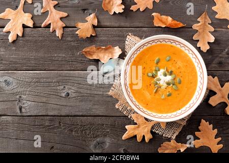 Cremige Butternut-Kürbissuppe, Tischszene über dem Kopf mit Herbstblättern auf rustikalem Holzhintergrund Stockfoto