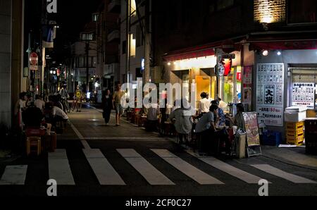 An einem Sommerabend versammeln sich Gäste an und um behelfsmäßige Sitze und Tische außerhalb eines Yakitori-Restaurants in Tokio, Japan Stockfoto