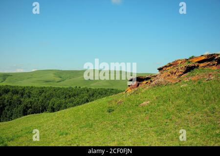 Eine alte Mauer, die entlang der Spitze eines hohen grasbewachsenen Hügel mit Blick auf ein malerisches Tal verläuft. Bergkette Truhen, Chakassien, Südsibirien, Russi Stockfoto