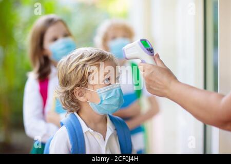 Temperaturkontrolle und ärztliche Untersuchung in der Schule. Kind in Gesichtsmaske in der Klasse in covid-19 Ausbruch. Lehrer mit Thermometer am Eingang der Vorschule. S Stockfoto