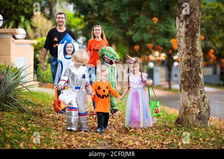 Kind in Halloween-Kostüm. Asiatische und kaukasische Kinder und Eltern mit gemischten Rassen tricksen oder gönnen sich auf der Straße. Kleiner Junge und Mädchen mit Kürbislaterne und Dose Stockfoto