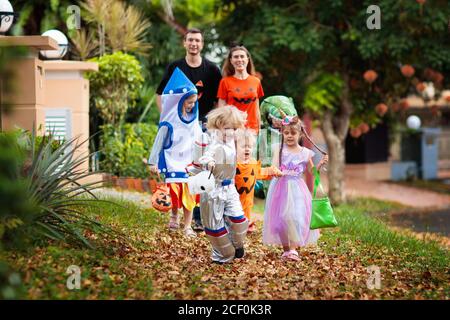 Kind in Halloween-Kostüm. Asiatische und kaukasische Kinder und Eltern mit gemischten Rassen tricksen oder gönnen sich auf der Straße. Kleiner Junge und Mädchen mit Kürbislaterne und Dose Stockfoto