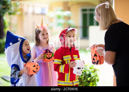 Kinder Trick or Treat in Halloween Kostüm. Kinder in bunten verkleiden sich mit Süßigkeiten Eimer auf Vorstadtstraße. Kleiner Junge und Mädchen Trick oder Behandlung wi Stockfoto