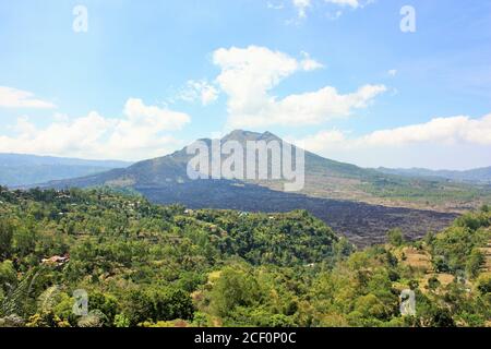 Mount Batur Vulkan, mit Bäumen und grünen Laub im Vordergrund und schwarzen vulkanischen Gesteinsfeld in Bali, Indonesien Stockfoto