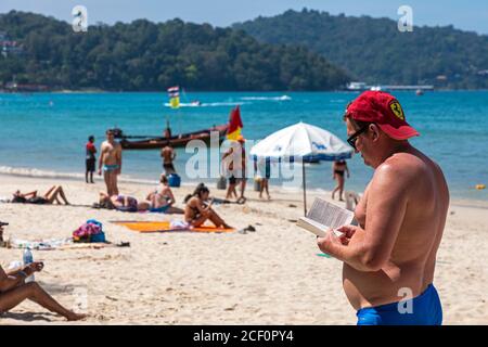 Russischer Tourist, Lesen und Sonnenbaden im Stehen am Patong Beach, Phuket, Thailand Stockfoto