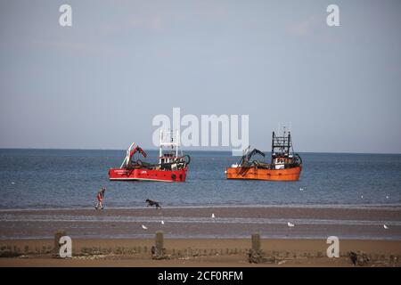 Hunstanton, Großbritannien. September 2020. Fischerboote auf See, wie eine Person spielt mit ihrem Hund an einem schönen sonnigen Tag heute in Hunstanton in Norfolk, Großbritannien. Kredit: Paul Marriott/Alamy Live Nachrichten Stockfoto