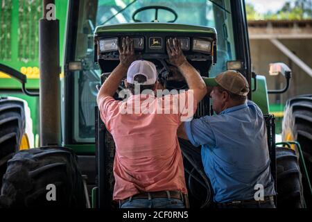 Schirmer Farms (Batesville) Operations Manager Brandon Schirmer, unterstützt von Farmbesitzer und Vater Ernie Schirmer, stellt ihren John Deere Traktor wieder zusammen, in der Nähe von San Antonio, TX, am 11. August 2020. Sie führen notwendige Reparaturen und Wartungsarbeiten an landwirtschaftlichen Geräten durch, um sich auf die bevorstehende Baumwollernte vorzubereiten. Stockfoto