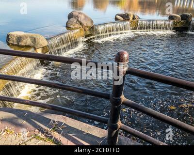 Kleiner künstlicher Wasserfall mit Steinen am See im öffentlichen Park. Sonniger Herbsttag Stockfoto
