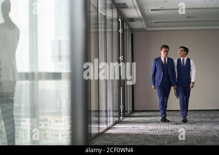 Zwei asiatische Führungskräfte diskutieren Geschäfte, während sie im Büro gehen Stockfoto