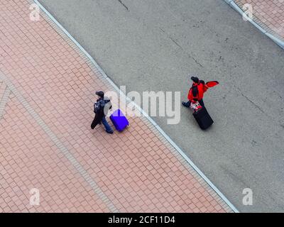 Männer mit Koffern auf Rädern gehen auf der Straße entlang. Blick von oben Stockfoto