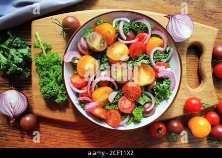 Frischer grüner Salat mit Kirschtomaten, Kohl Kale, Zwiebeln auf Schneidebrett. Holzhintergrund Stockfoto