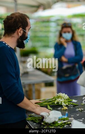 Cremona, Italien - September 2020 Blumen- und Pflanzenverkäufer auf dem Wochenmarkt. Gärtner und Kunden tragen Gesichtsmaske und halten Abstand- Stockfoto