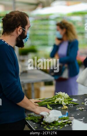 Cremona, Italien - September 2020 Blumen- und Pflanzenverkäufer auf dem Wochenmarkt. Gärtner und Kunden tragen Gesichtsmaske und halten Abstand- Stockfoto