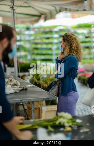 Cremona, Italien - September 2020 Blumen- und Pflanzenverkäufer auf dem Wochenmarkt. Gärtner und Kunden tragen Gesichtsmaske und halten Abstand- Stockfoto