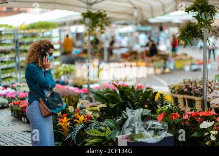 Cremona, Italien - September 2020 Blumen- und Pflanzenverkäufer auf dem Wochenmarkt. Gärtner und Kunden tragen Gesichtsmaske und halten Abstand- Stockfoto