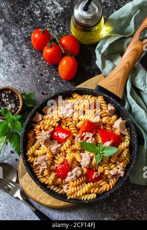 Gesundes Mittagessen. Fusilli-Pasta mit Thunfisch aus der Dose, gegrillte Paprika und Tomaten in einer Pfanne auf einer Steinplatte. Stockfoto