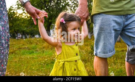 Nettes kleines Mädchen nehmen Hände mit ihrem Vater. Walking with Kids Konzept Bild. Kleines Mädchen hält die Hände mit ihren Eltern. Lächelndes Baby im Kleid. Stockfoto