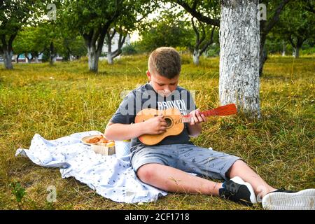 Kleiner Junge Gitarrist im Freien. Junge auf Stadtpark Sommerwiese genießen Tag Gitarre spielen. Stockfoto