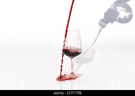 Sommelier gießt Rotwein von Dekanter zu Weinglas auf weißem Hintergrund. Verschüttet Rotwein am Glas vorbei auf einem weißen Tisch. Stockfoto