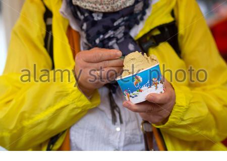 Eine Frau in einer gelben Regenjacke isst aus einer Eiswanne in Weimar Stockfoto