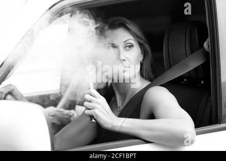 Hübsche Frau, die beim Autofahren die E-Zigarette raucht Stockfotografie