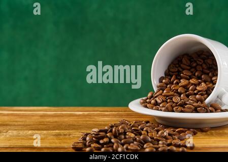 Internationaler Tag des Kaffees Konzept. Nahaufnahme weiße Kaffeetasse voller Kaffeebohnen auf dunkelgrünem Hintergrund. Stockfoto
