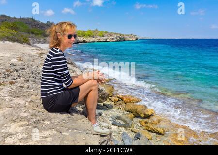 Kaukasische Frau mittleren Alters sitzt an der Küste der Niederländischen Antillen Stockfoto