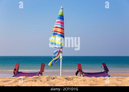 Farbenfroher Sonnenschirm mit Liegen am Strand mit blauem Meer Stockfoto