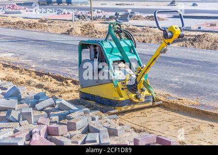 Vibrierende Maschine auf Sand neben der neuen Straße in der Straße Konstruktion Stockfoto