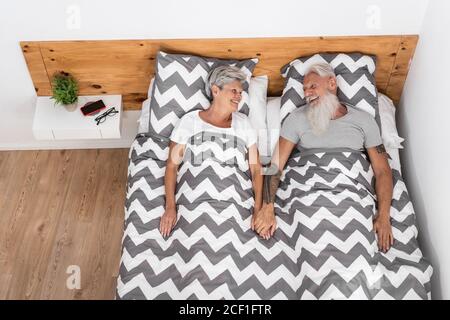 Glücklicher älterer Ehemann, der seine Frau an der Hand hält. Ältere Menschen mit Spaß im Bett liegen - Fokus auf Gesichter - ältere fröhliche Lebensstile Konzept Stockfoto