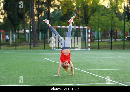 Mädchen in einem roten T-Shirt ist in der Gymnastik auf dem Sportplatz beschäftigt. Stockfoto