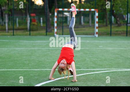 Mädchen in einem roten T-Shirt ist in der Gymnastik auf dem Sportplatz beschäftigt. Stockfoto