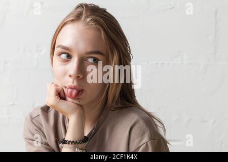 Lustige blonde Teenager-Mädchen zeigt Zunge, Nahaufnahme Studio-Porträt mit natürlichem Licht über weiße Wand Stockfoto