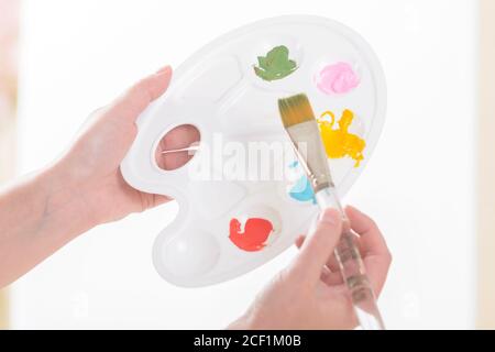 Hände einer Künstlerin, die in einem Atelier Palette mit verschiedenen Farben und Pinsel hält. Stockfoto