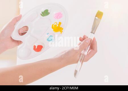 Hände einer Künstlerin, die in einem Atelier Palette mit verschiedenen Farben und Pinsel hält. Stockfoto