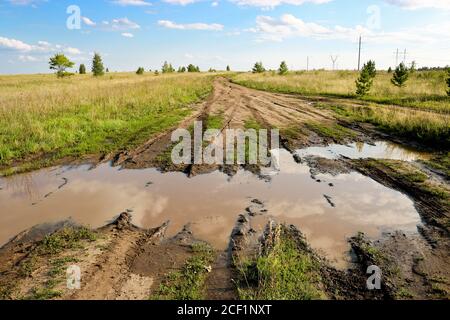 Sommerlandschaft - Feldweg mit einer großen Pfütze und Schlamm zwischen Wiesen. Die Ruhe der Landschaft. Stockfoto