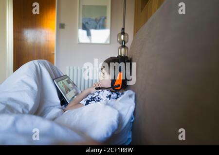 Junge mit Kopfhörer E-Learning mit digitalem Tablet im Bett Stockfoto