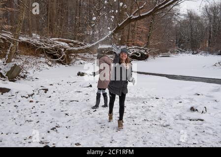 Mädchen wirft einen Schneeball in der Nähe eines Stromes mit ihr Schwester im Hintergrund Stockfoto