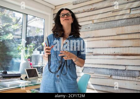 Frau mit Smartphone, die im sonnigen Heimbüro arbeitet Stockfoto