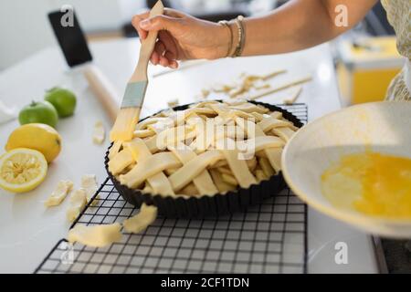 Nahaufnahme Frau putzt Gitterpastete mit Eigelb in Küche Stockfoto