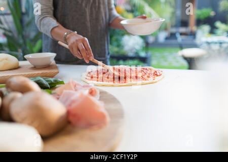 Frau verteilt Tomatensauce auf Pizzateig Stockfoto