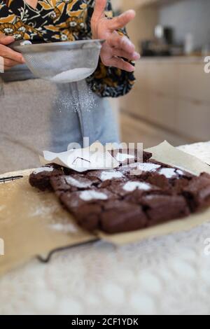 Frau streut Puderzucker Herzen über gebackene Brownies in der Küche Stockfoto