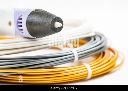 Nahaufnahme der Reihe von bunten gerollten Kabel und Kinder 3D-Druckstift isoliert auf weiß. Drei helle Filament Kunststoff liegen drinnen, Studio b Stockfoto