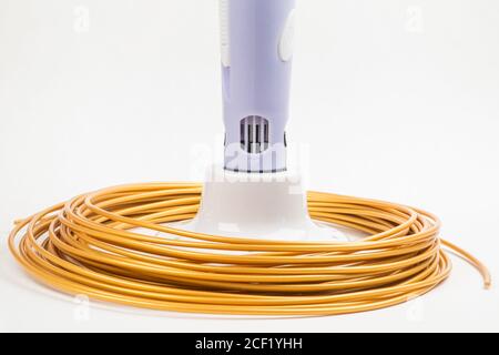 Nahaufnahme von golden gerollten Kabeln um Kinder 3D-Druckstift isoliert auf weiß. Helles Filament Kunststoff liegt drinnen, Studio Hintergrund. Kontra Stockfoto