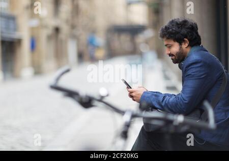 Geschäftsmann mit Fahrrad mit Smartphone auf der Stadtstraße Stockfoto